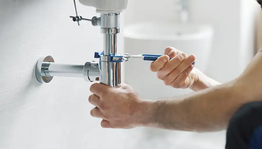 Technician repairing a leaking pipe under a residential kitchen sink